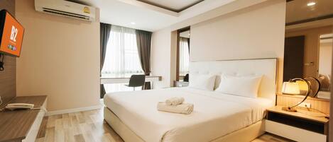 A hotel room with a large bed, a desk, a chair, a TV, and an air conditioning unit.