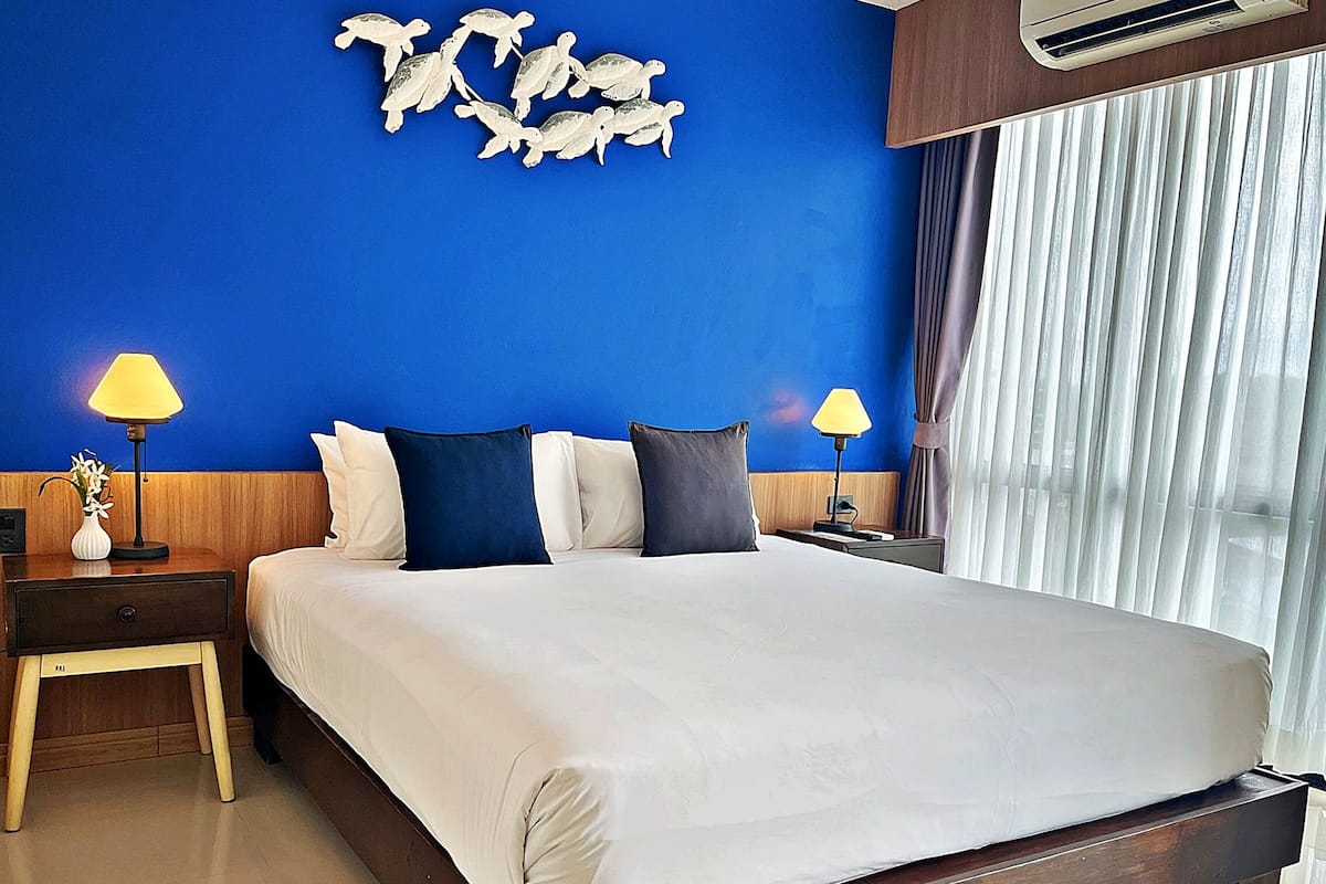 A hotel room with a large bed, two bedside tables with lamps, a wall art of sea turtles, and a window with curtains.