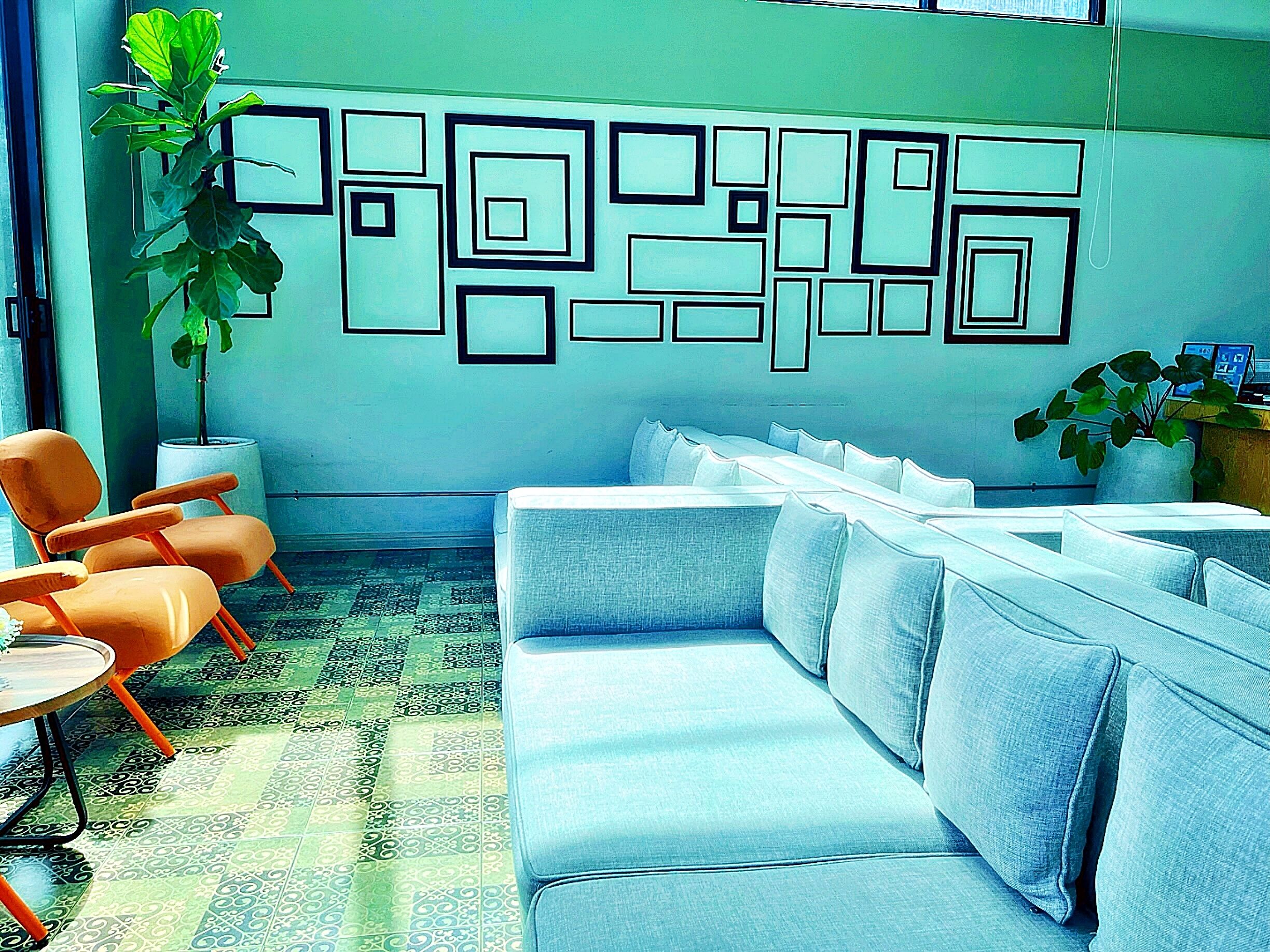 Un área de espera moderna con un sofá azul, sillas naranjas y un diseño geométrico en la pared.