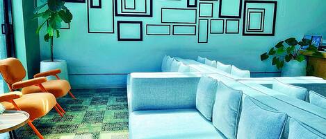 Un área de espera moderna con un sofá azul, sillas naranjas y un diseño geométrico en la pared.