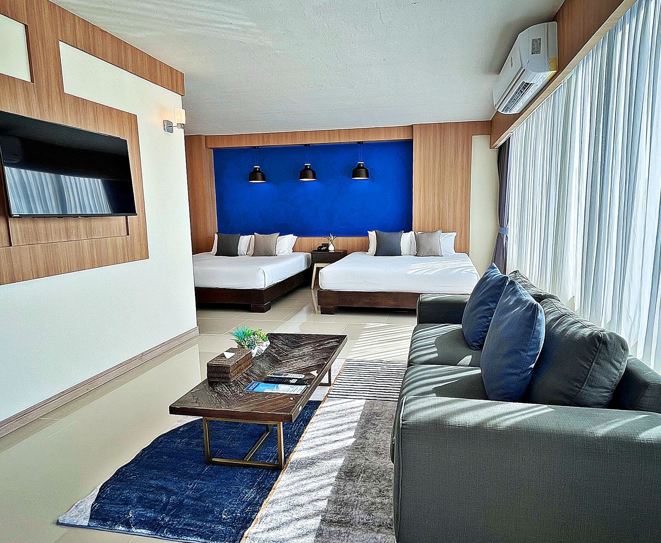 Een moderne hotelkamer met twee eenpersoonsbedden, een slaapbank, een salontafel en een aan de muur bevestigde televisie.