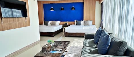 A modern hotel room with two single beds, a sofa, a coffee table, and a TV mounted on the wall.