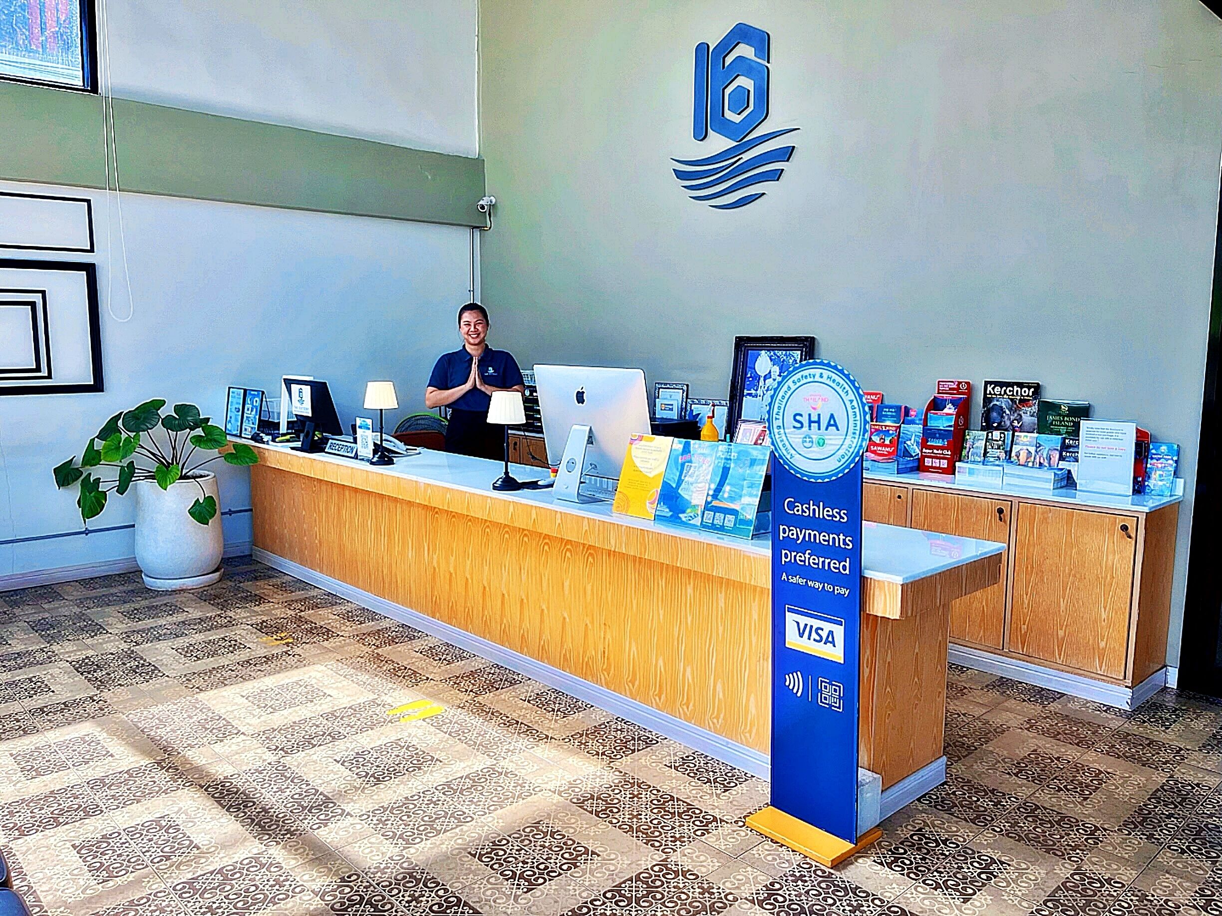 Een receptiebalie met een blauw bord waarop staat dat contactloze betalingen de voorkeur hebben, een betaalterminal voor VISA-kaarten en informatiefoodrukkruisjes.