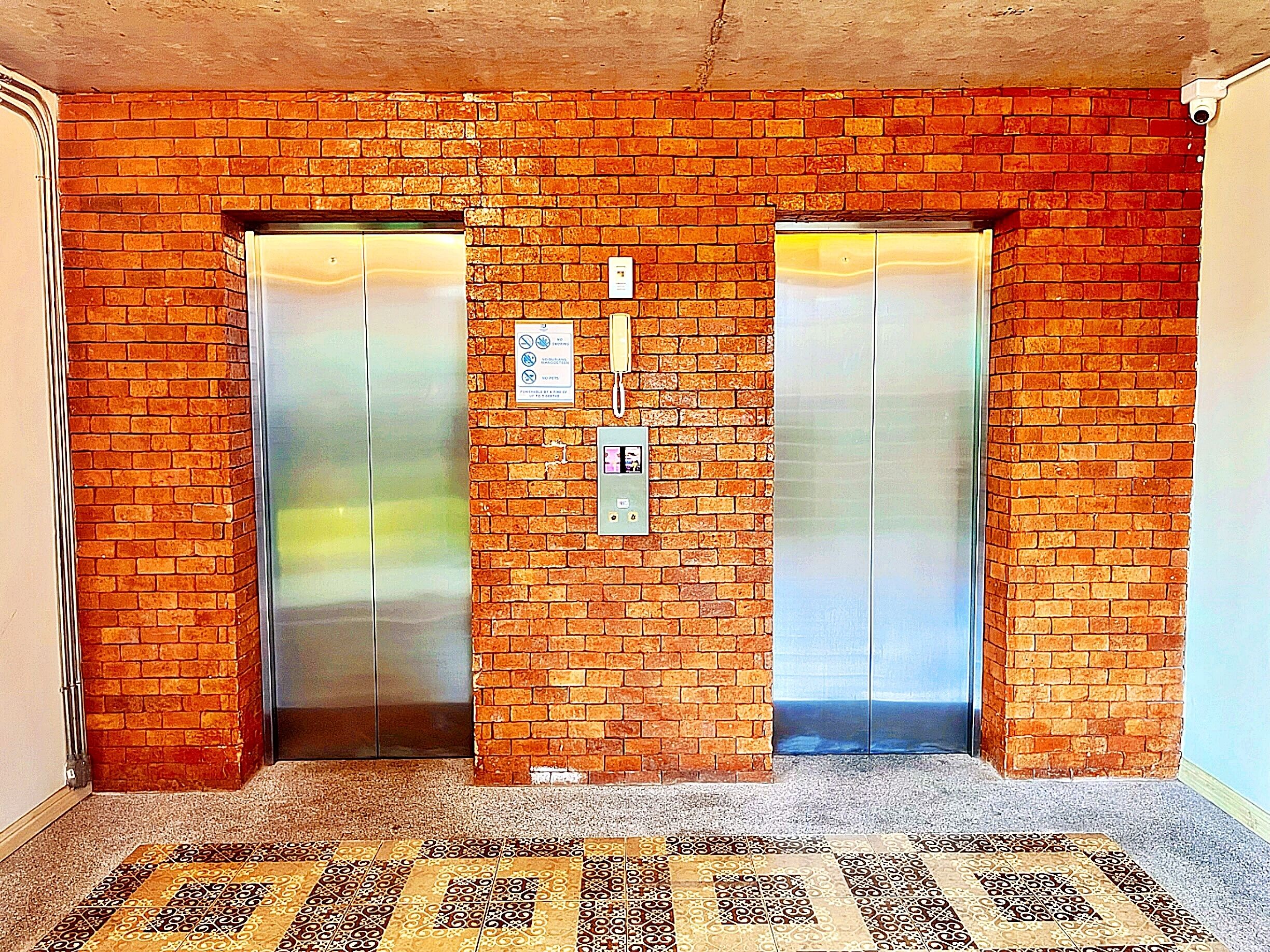 Un ascensor con pared de ladrillo, dos puertas y un suelo de baldosas con diseño.