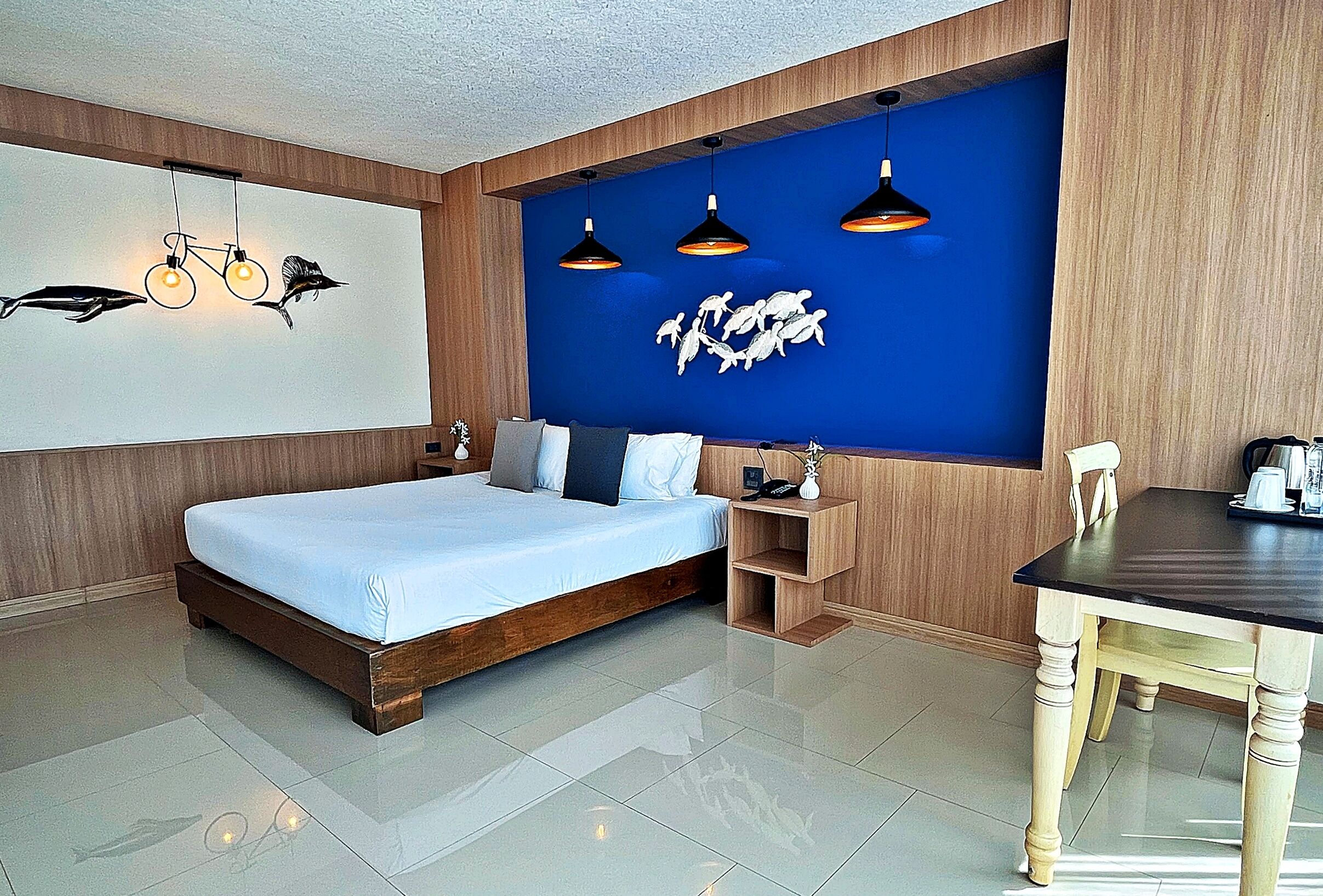 A modern bedroom with a large bed, a wooden nightstand, a desk, and a blue accent wall with wall art.
