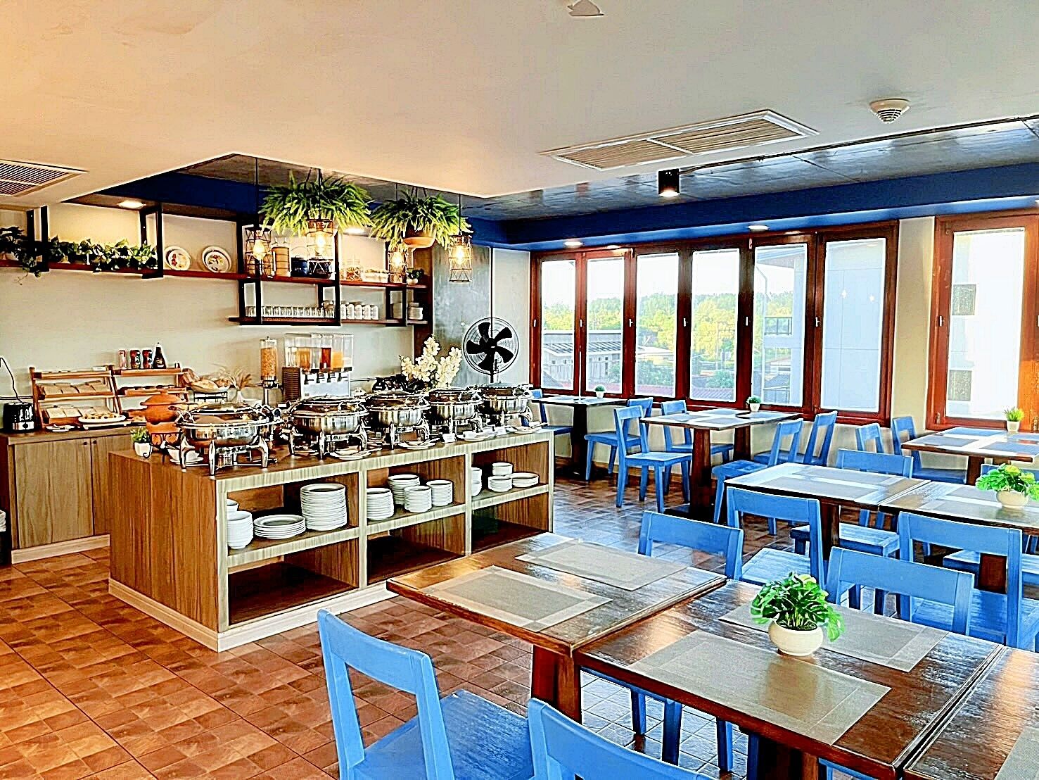 Un restaurante con mesas de buffet, sillas azules y ventanas amplias.