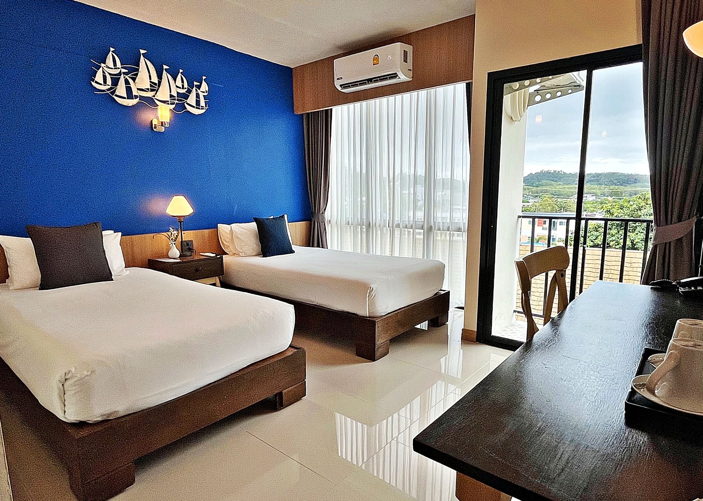 Habitación de hotel con dos camas, un escritorio, una lámpara y vistas al exterior.