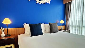 A hotel room with a large bed, two bedside lamps, a nightstand with a vase of flowers, and a blue wall with a decorative wall art piece.