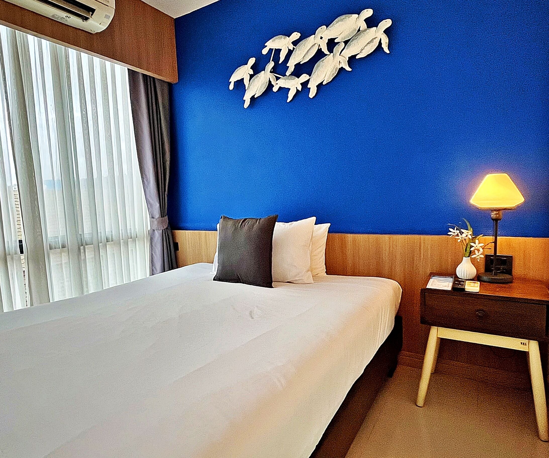 Una habitación de hotel con una cama grande, una mesita de noche con una lámpara y una decoración de tortugas marinas.