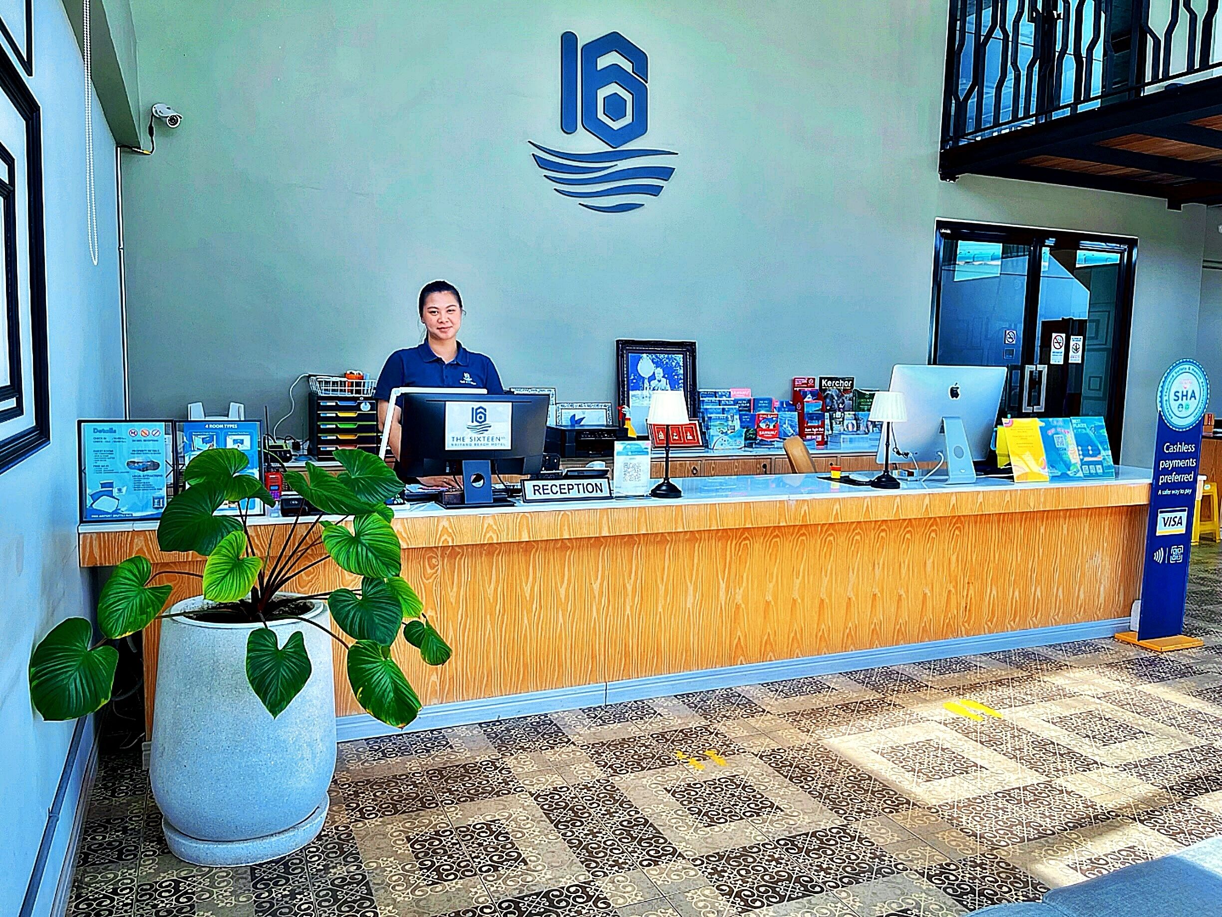A reception desk with a receptionist, a computer, a sign indicating '4 ROOM TYPE', and a logo on the wall.