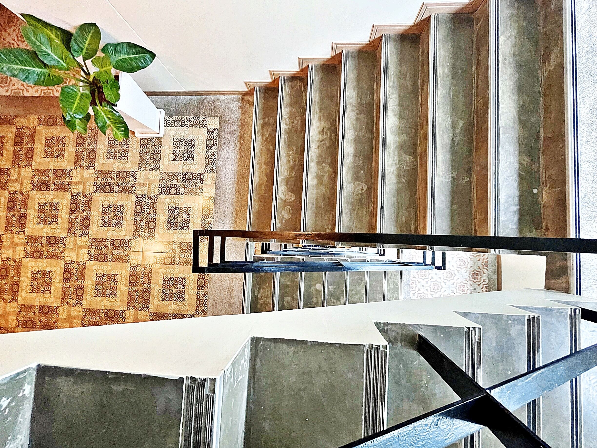 A modern staircase with a geometric design, a patterned wall, and a hanging plant.
