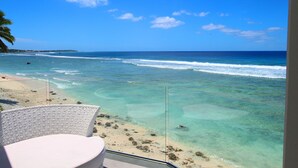 A beach view with clear turquoise water, a sandy shore, and a white chair. - Ocean Spray Villas (Rarotonga)
