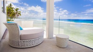 A balcony with a white wicker sofa and ottoman, overlooking a beach with clear turquoise water and palm trees. - Ocean Spray Villas (Rarotonga)