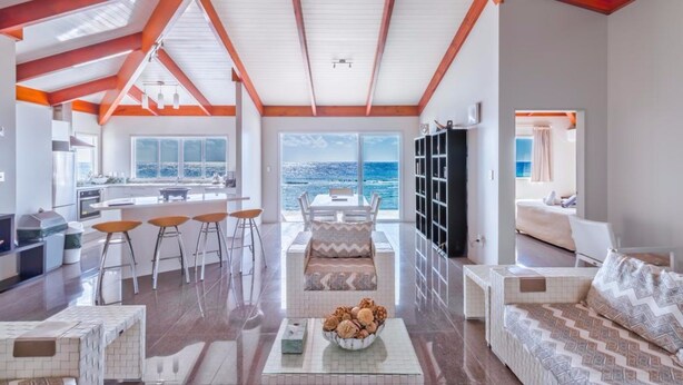 A spacious living area with a high ceiling, a kitchen, a dining area, and a view of the ocean. - Ocean Spray Villas (Rarotonga)