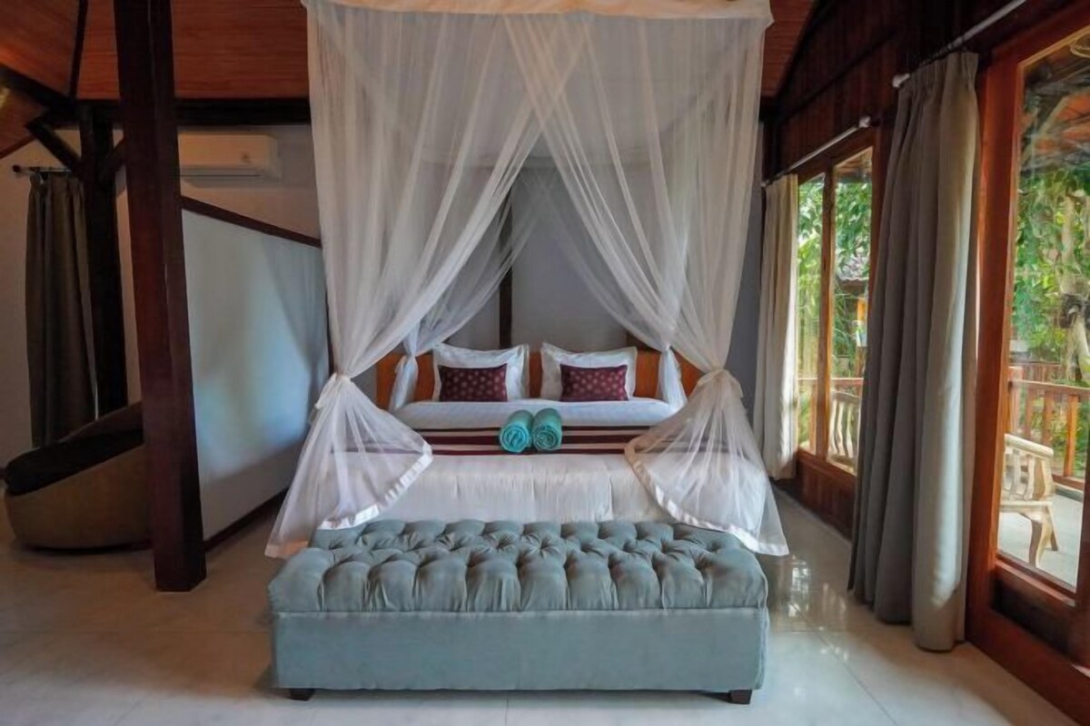 A bedroom with a canopy bed, a bench, and a view of the outdoors.