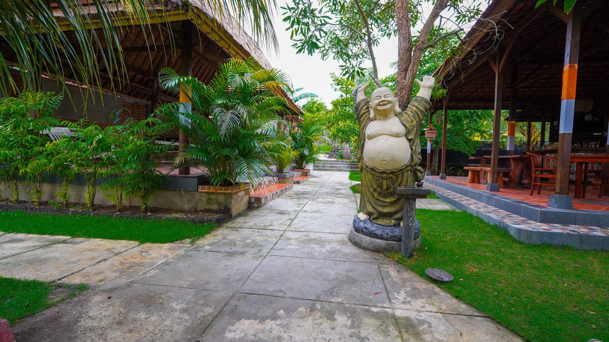 A pathway leading to a covered outdoor area with a statue, surrounded by lush greenery and potted plants.