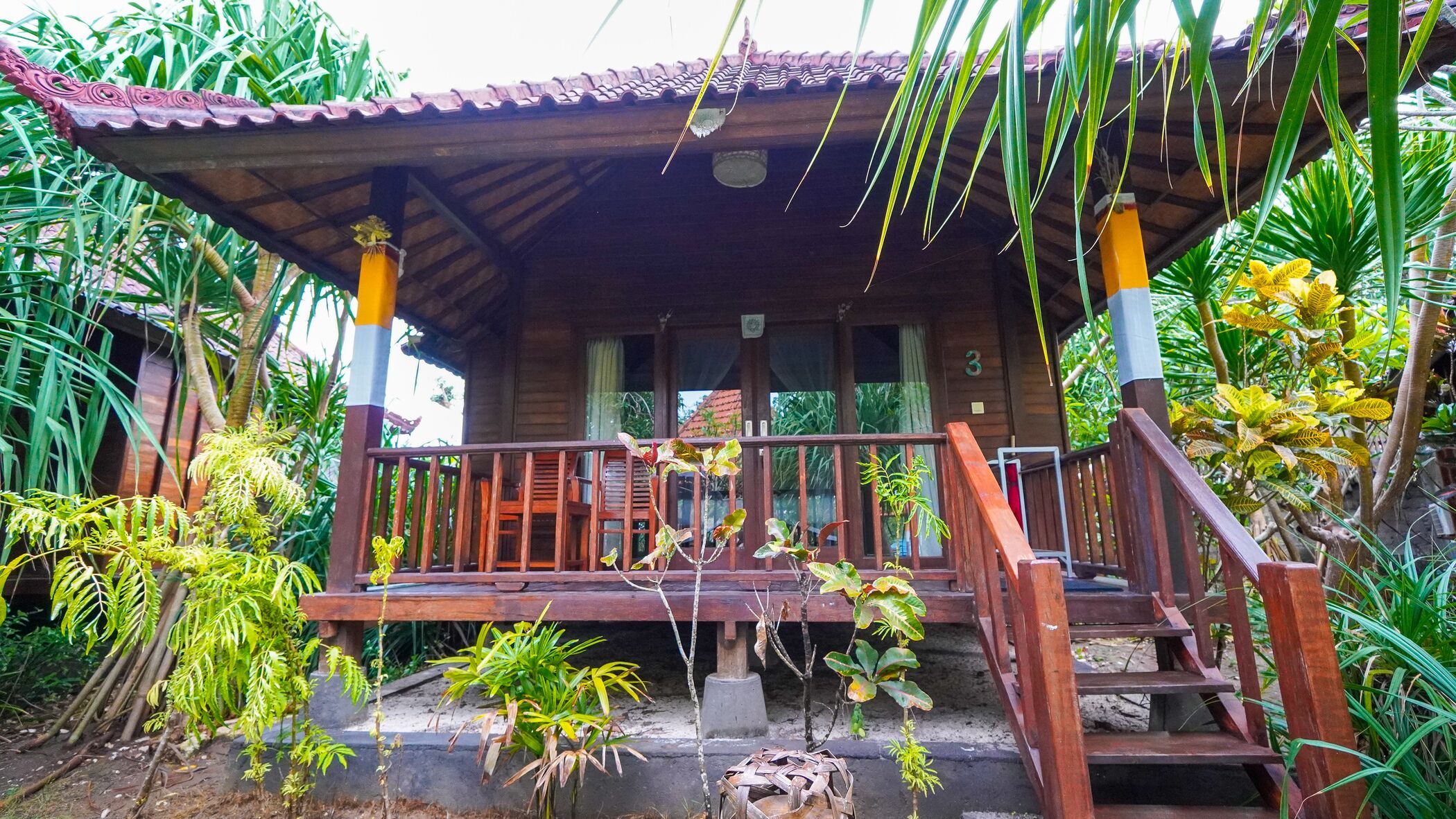 A wooden house with a porch, surrounded by tropical plants.