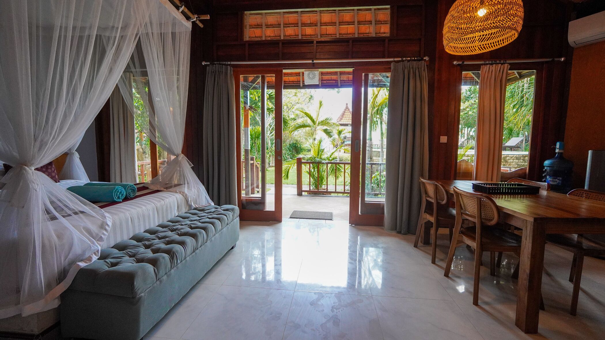 A room with a bed, a bench, a dining table, and a view of the outdoors.