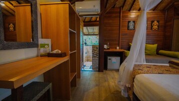 Quarto com cama, escrivaninha e uma pequena cozinha. Há uma janela com vista para o verde lá fora.