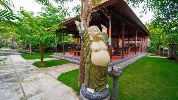 Una estatua de una figura con los brazos levantados, un área de estar al aire libre techada y un jardín cuidado.