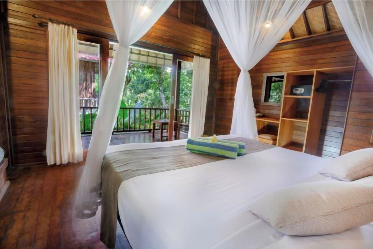 A bedroom with a wooden ceiling, a bed with white linens, a small window, and a balcony with a railing.
