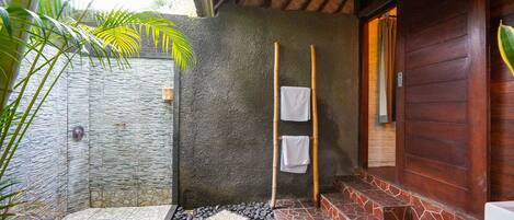 Un baño con paredes de piedra, una puerta de madera, una barra de cortina de ducha de bambú y un piso de baldosas.
