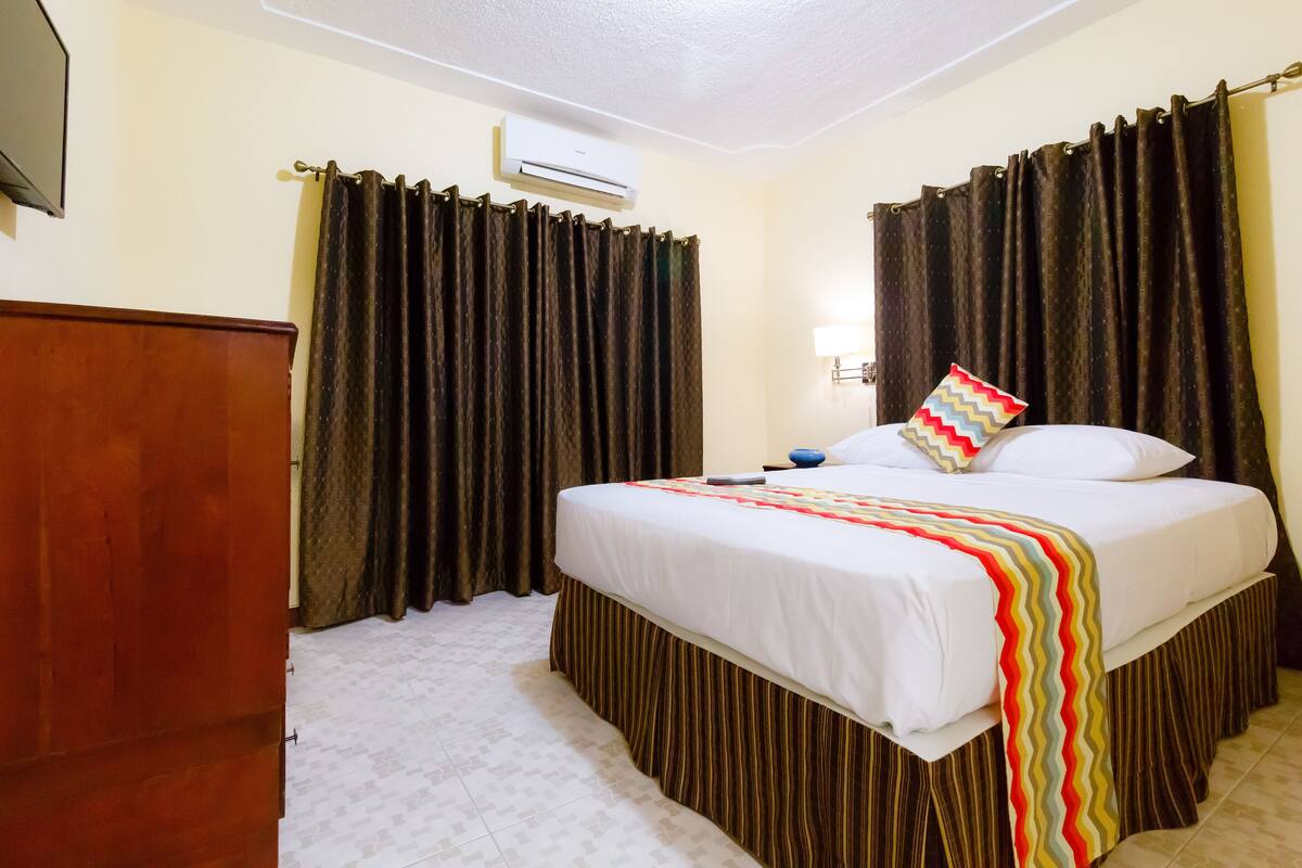 Une chambre d’hôtel avec un lit, des rideaux, un appareil de climatisation et une armoire en bois.