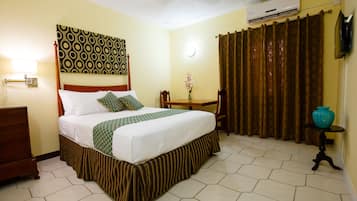 Habitación de hotel con cama, escritorio, silla, televisor y aire acondicionado.