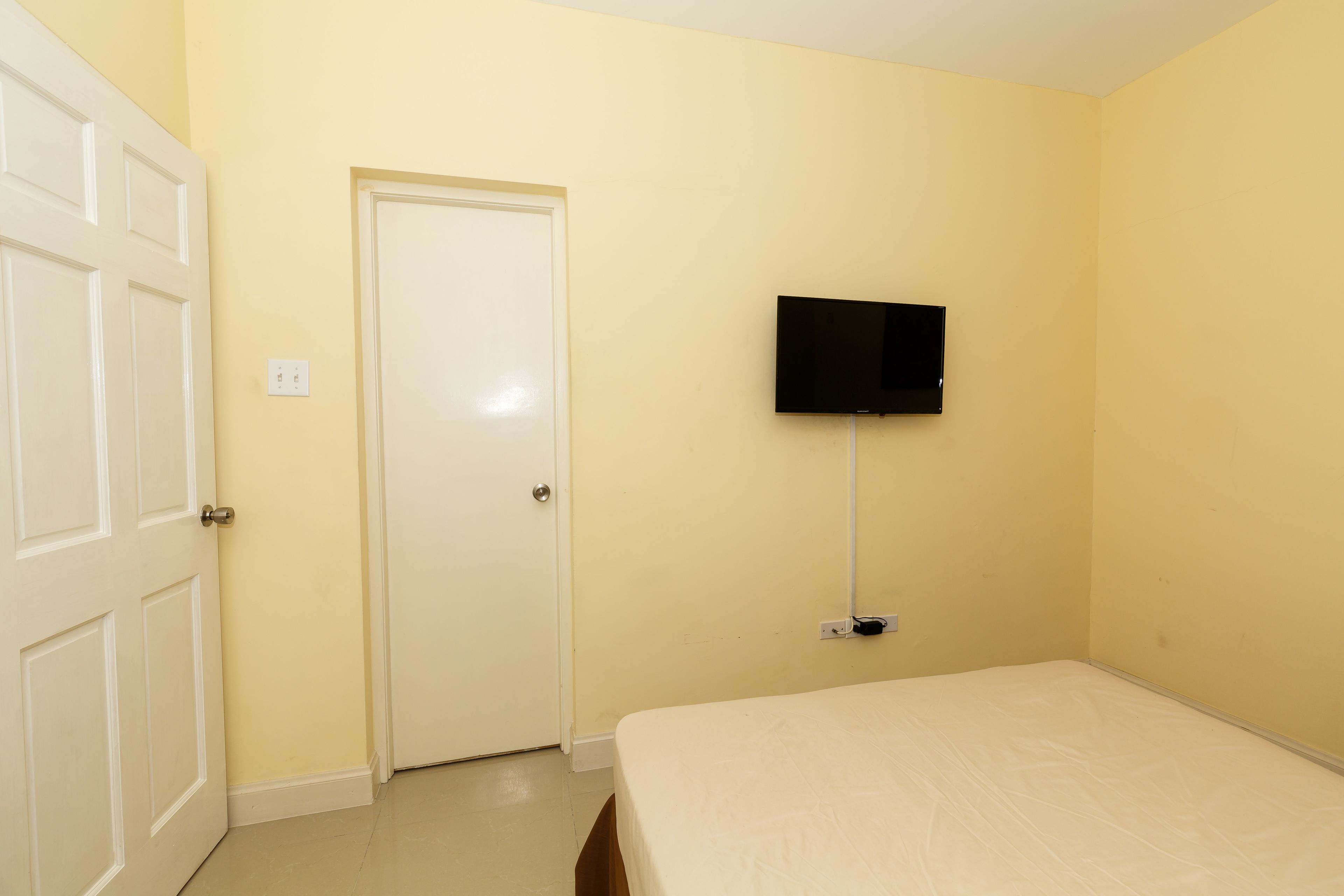 A room with a bed, a door, and a mounted TV.