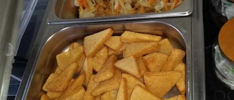 Buffet com bandejas de frango frito e salada de repolho, e um recipiente com batatas rústicas.