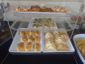 A buffet with various food items including pastries, sandwiches, and a bowl of fruit.