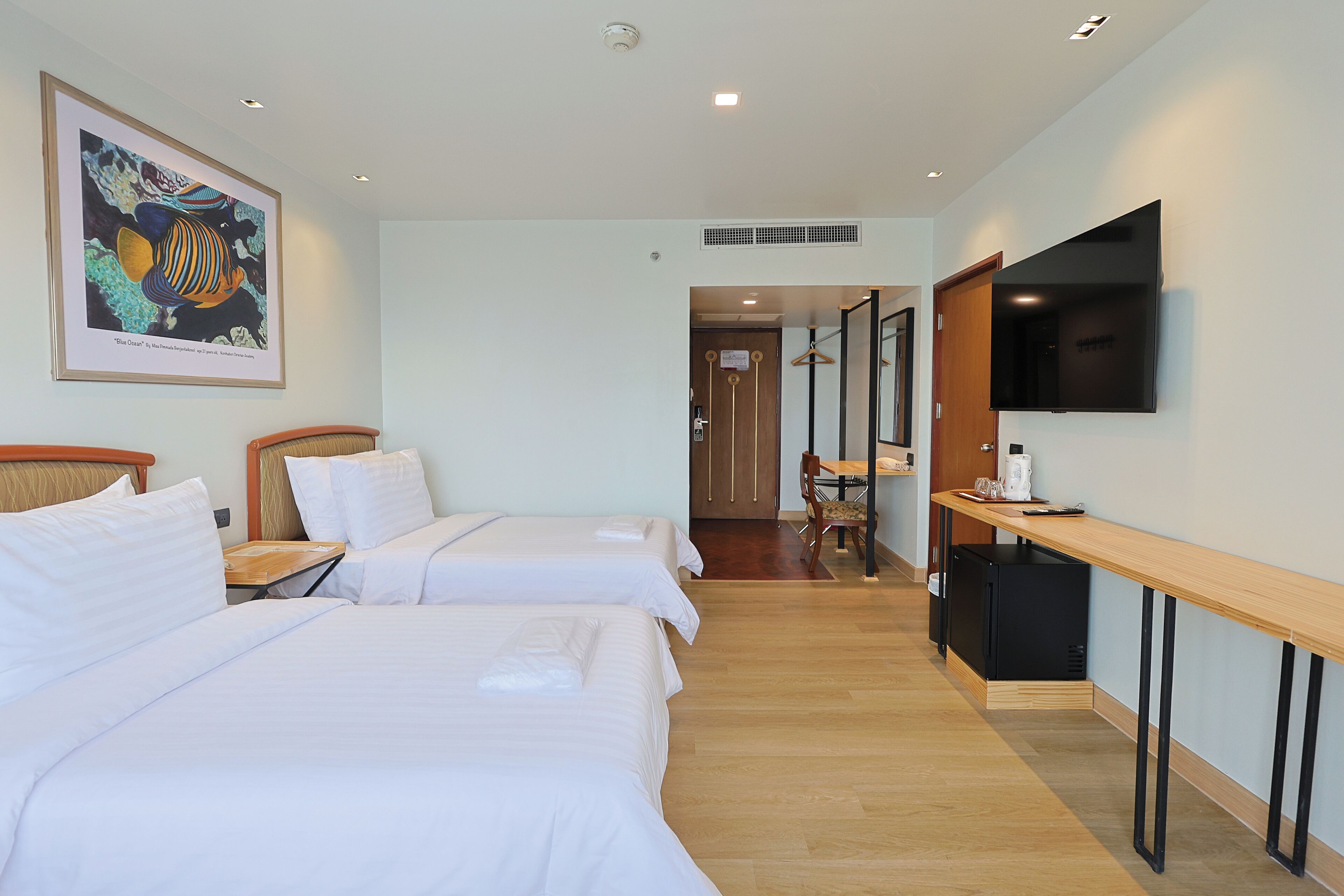 A hotel room with two beds, a flat-screen TV, a wooden desk, and a framed artwork on the wall.