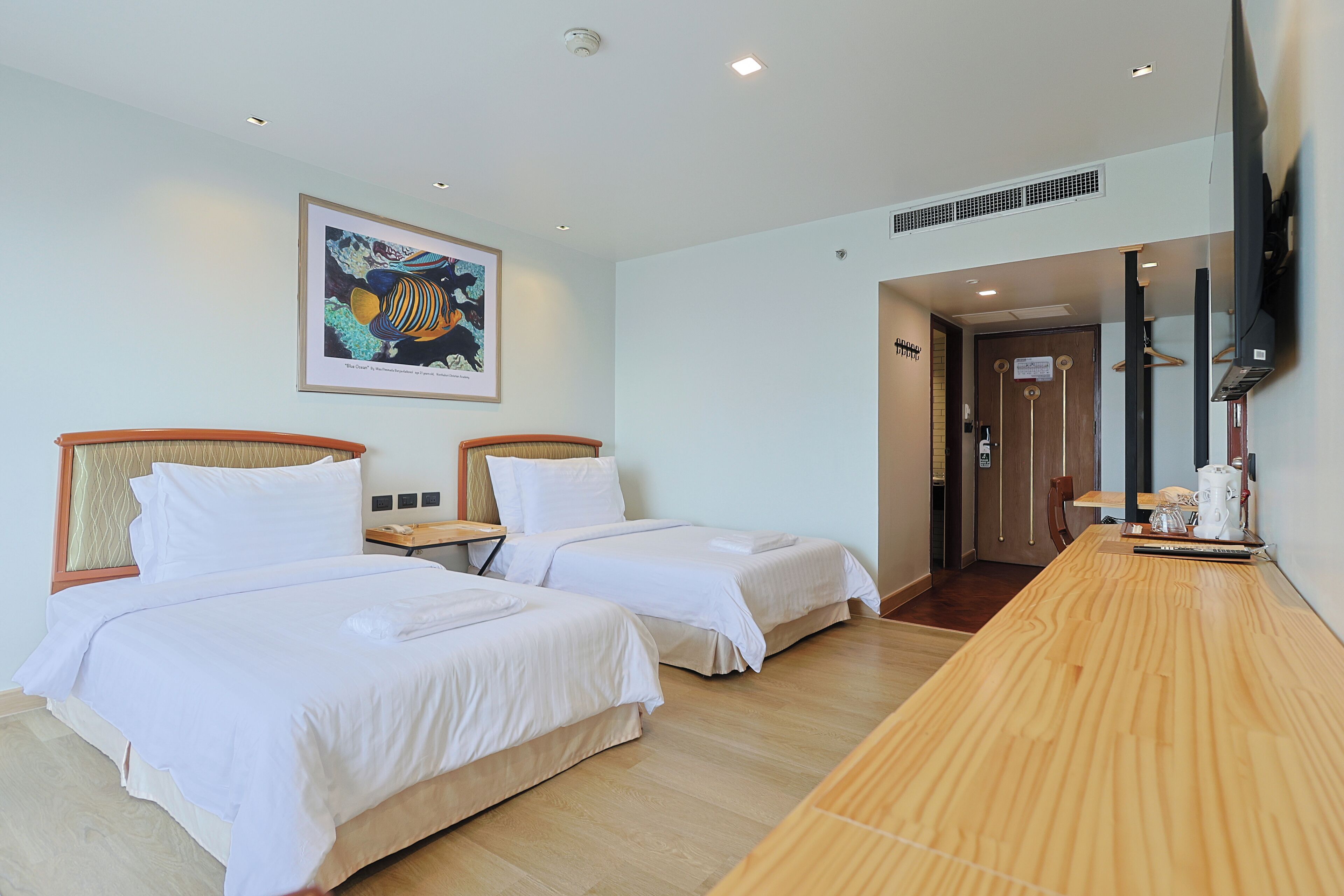 A hotel room with two beds, a wooden desk, a flat-screen TV, and a framed artwork on the wall.