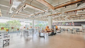 Un grand espace intérieur aménagé avec des tables et des chaises, de grandes fenêtres et une fresque murale.