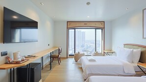 Une chambre d’hôtel avec deux lits, un bureau, une télévision et une grande fenêtre donnant sur la ville.