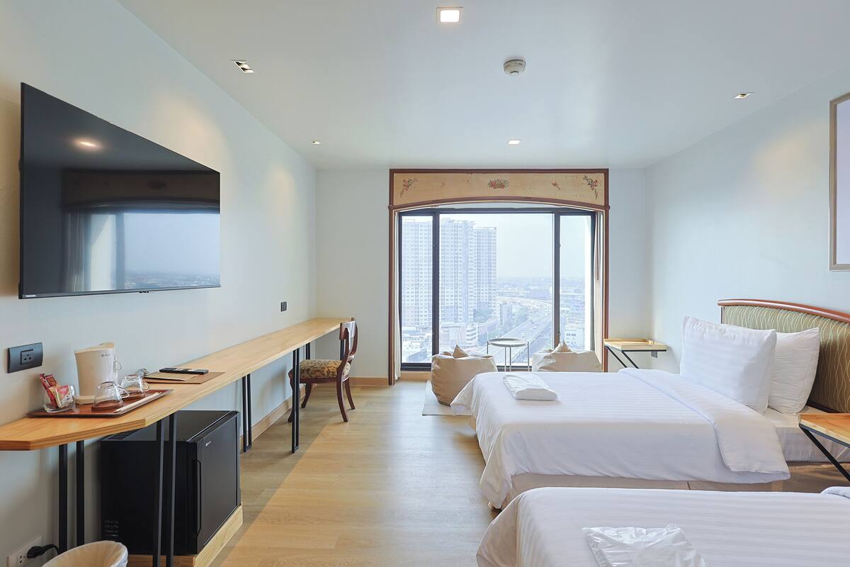 Hotelkamer met twee bedden, een bureau, een televisie en een groot raam met uitzicht over de stad.