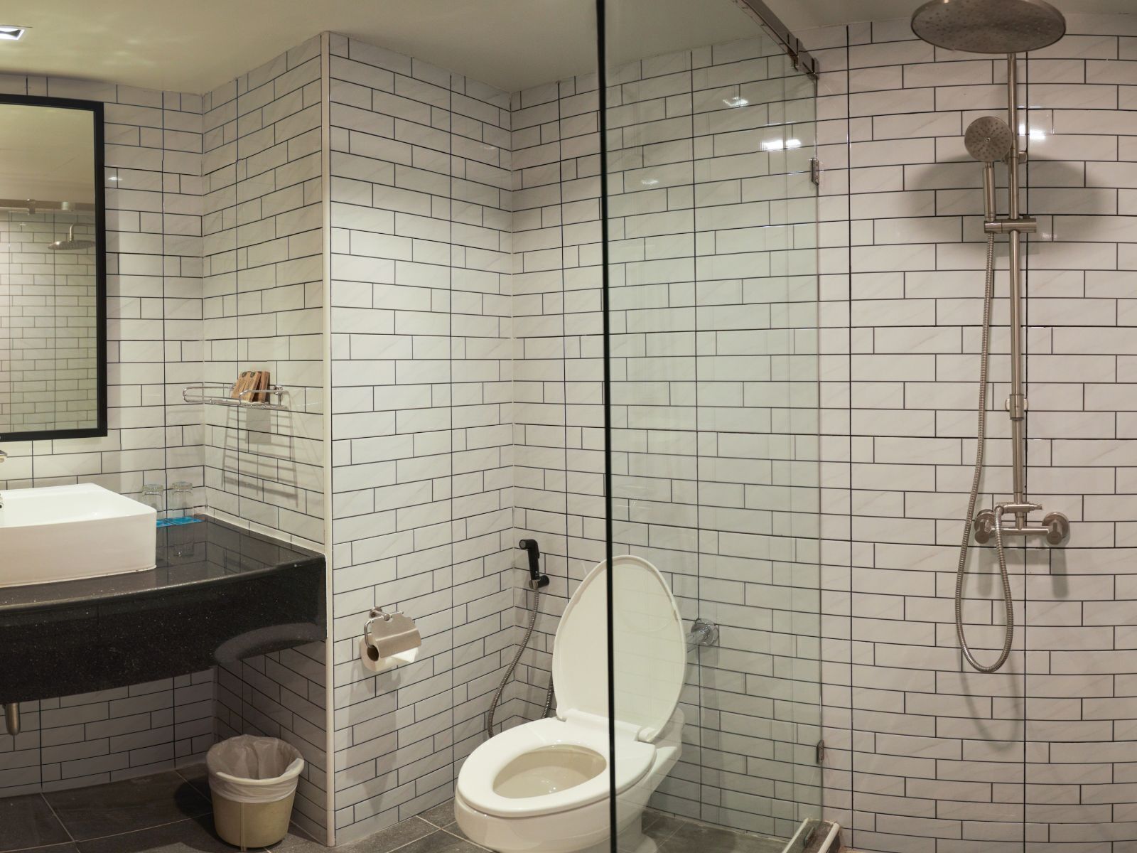 Een moderne badkamer met witte metrotegels, een zwart aanrechtblad met een wastafel, een douchecabine met glazen wanden en een toilet.
