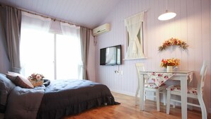 A bedroom with a bed, a TV, a table with chairs, and a window with curtains. - Edelweiss Pension (Pyeongchang)