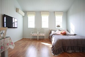 Un dormitorio con una cama, dos sillas, un televisor y tres ventanas.