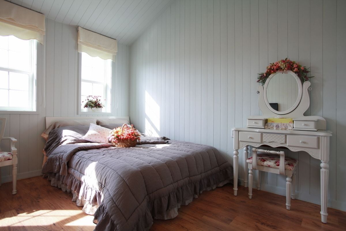 Une chambre à coucher avec un lit, une commode, un miroir et une fenêtre avec des rideaux.