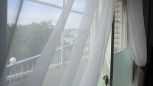 A view through a window with sheer curtains, revealing a balcony and a distant landscape. - Edelweiss Pension (Pyeongchang)