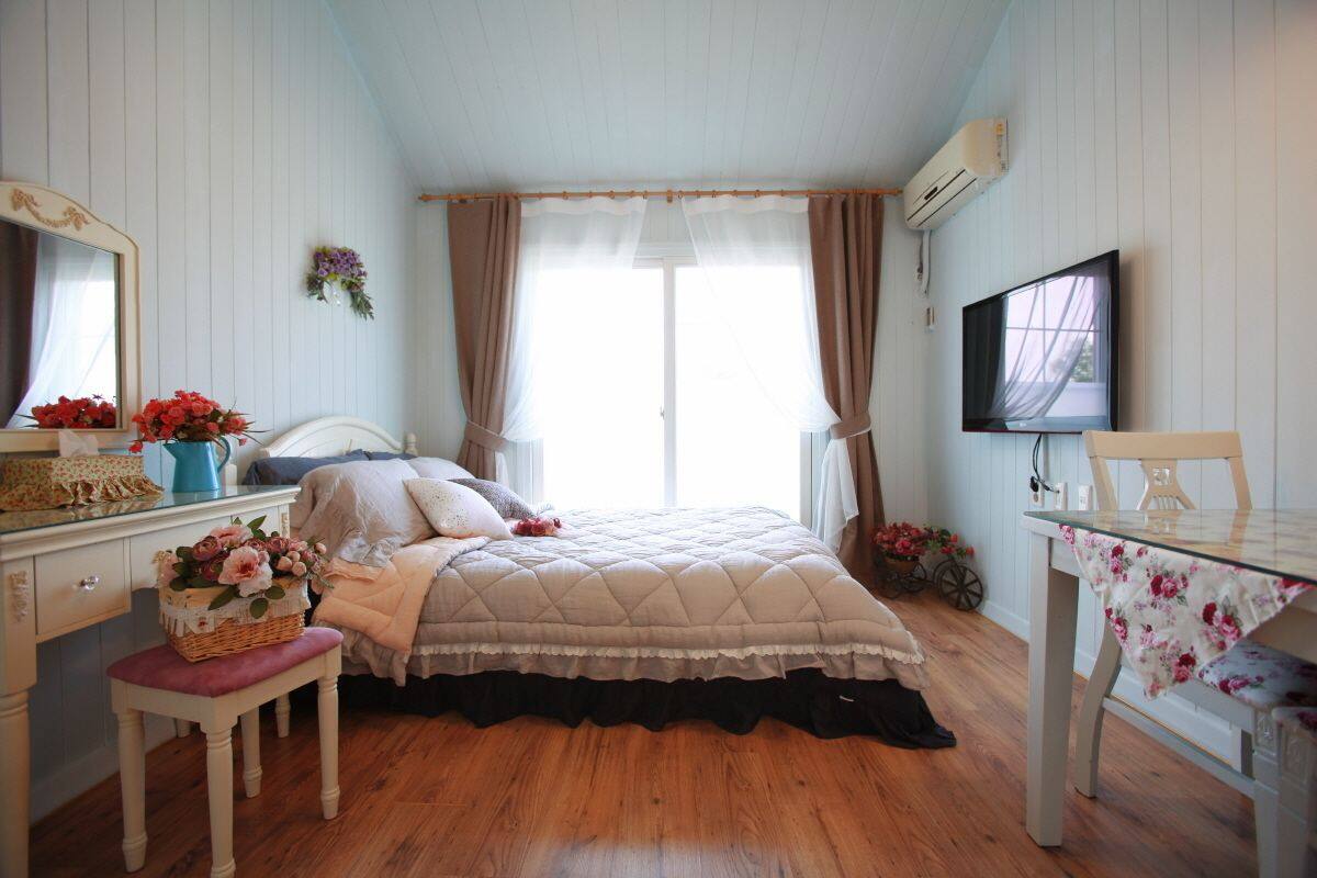 Une chambre à coucher comprenant un lit, une commode, un téléviseur et une fenêtre avec des rideaux.