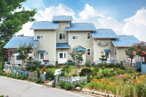 A two-story building with a blue roof, a signboard, and a well-maintained garden.
