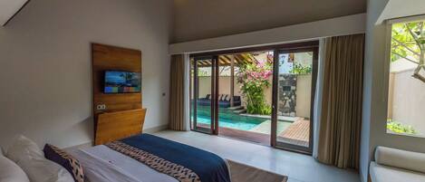 Een slaapkamer met een groot bed, een houten hoofdbord, een flatscreen televisie en een glazen schuifdeur naar een zwembad.