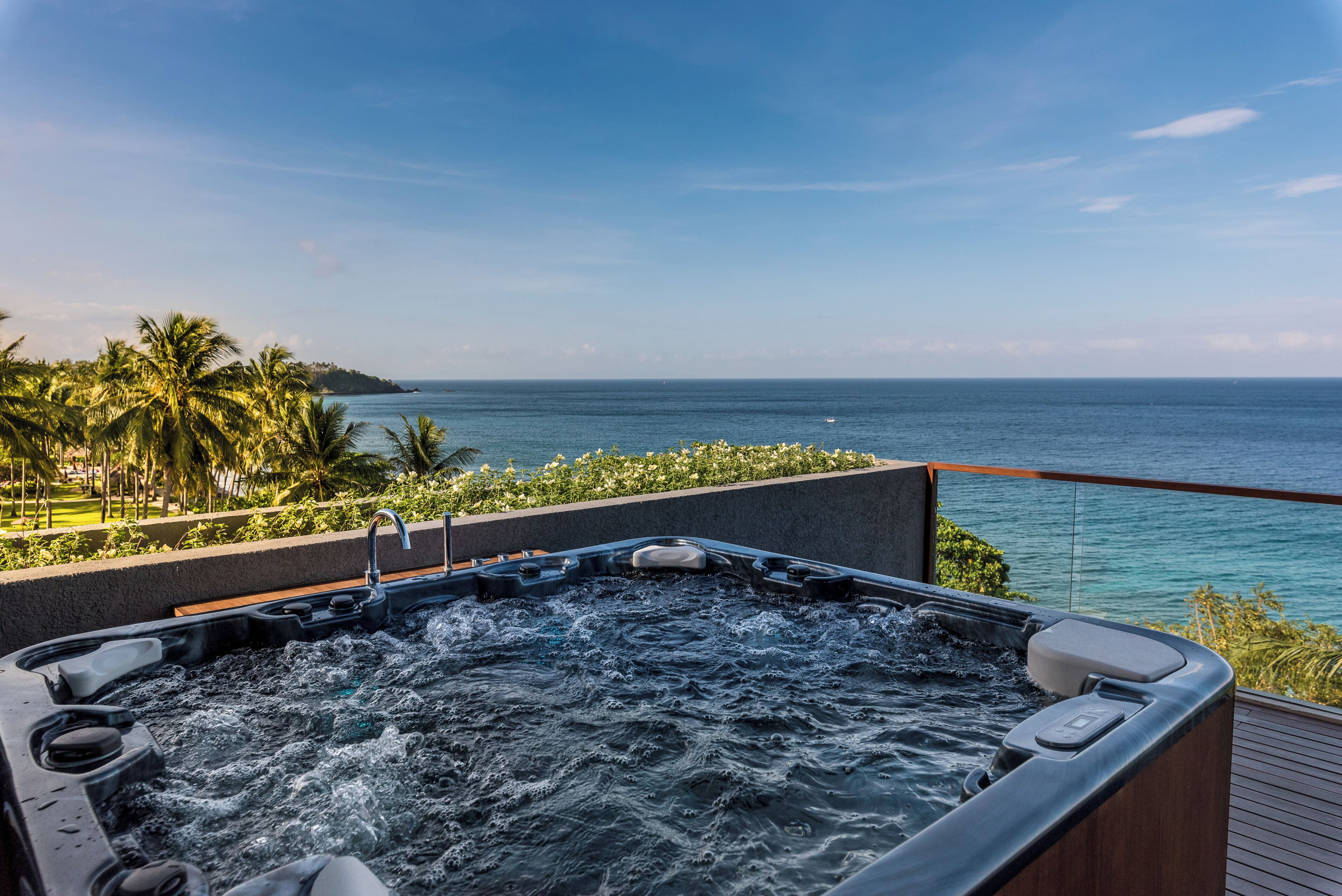 A hot tub on a deck with a view of the ocean and palm trees.