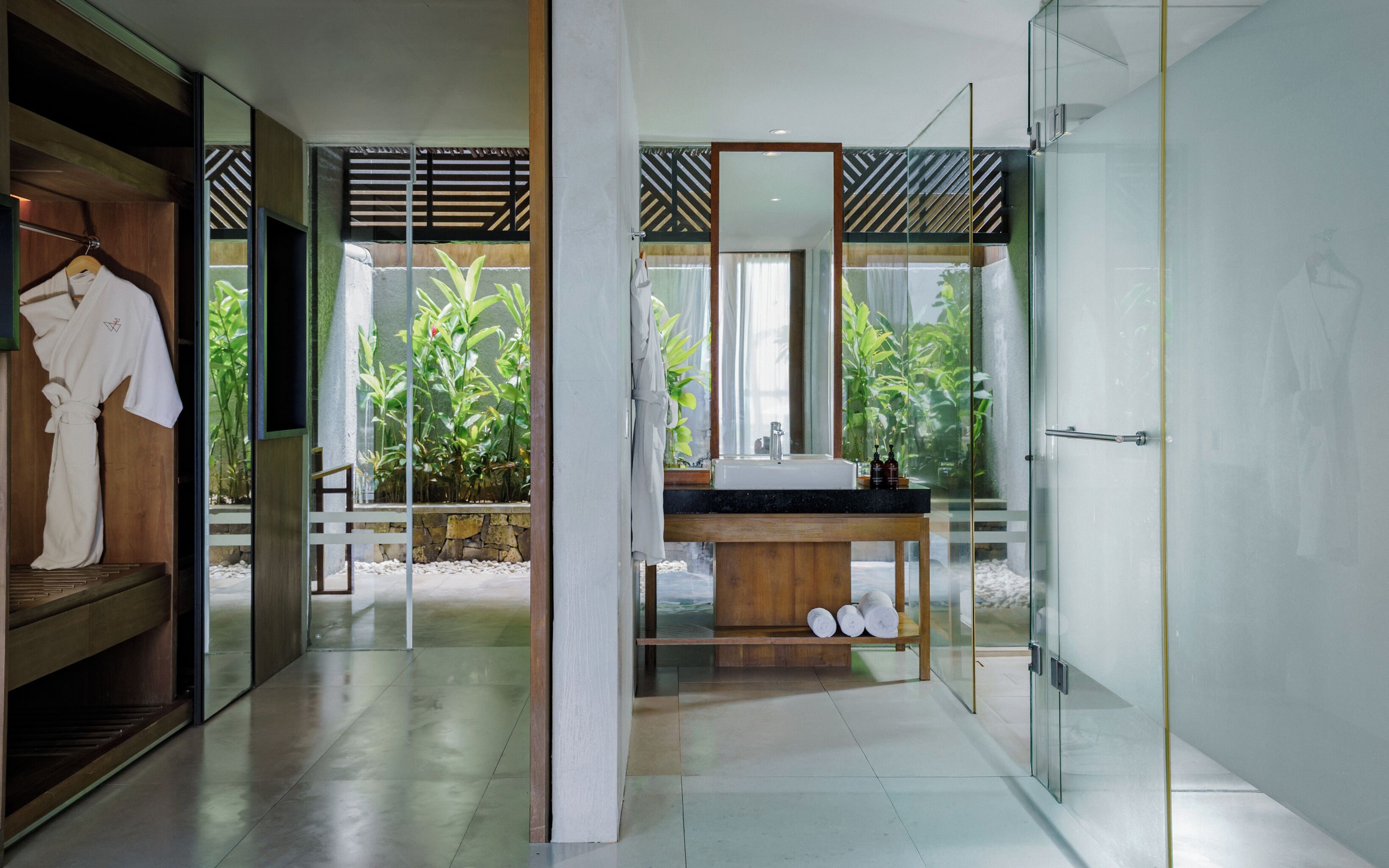 Een moderne badkamer met een glazen douche, een houten wastafelmeubel en uitzicht op groen buiten.
