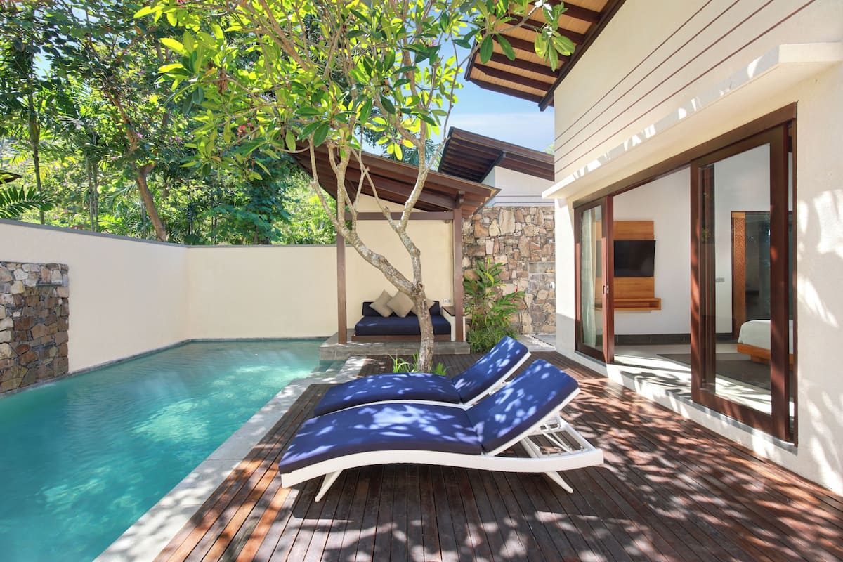 A poolside area with lounge chairs, a stone wall, and a wooden deck.
