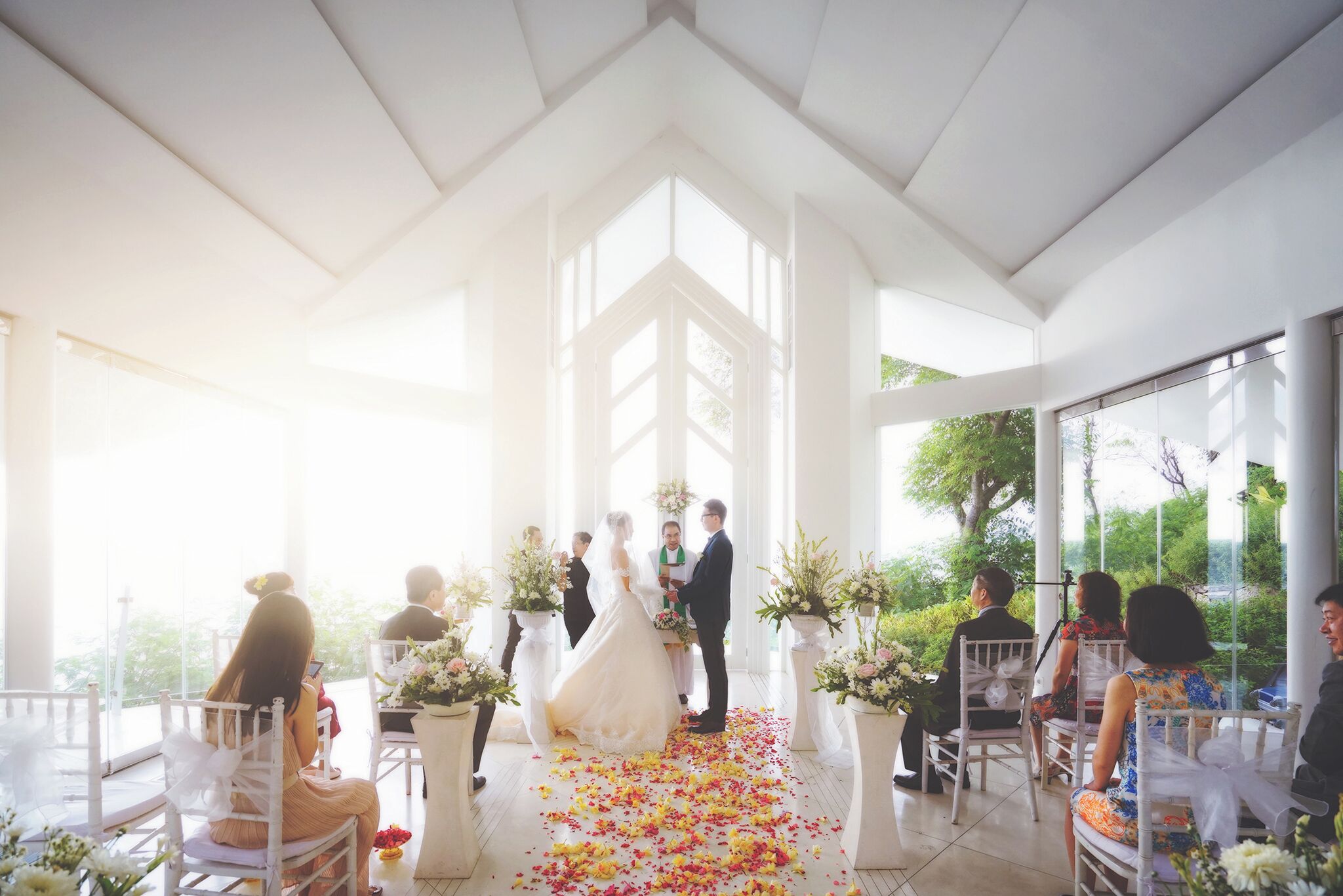 Une cérémonie de mariage avec une allée blanche et des invités assis sur des chaises blanches.