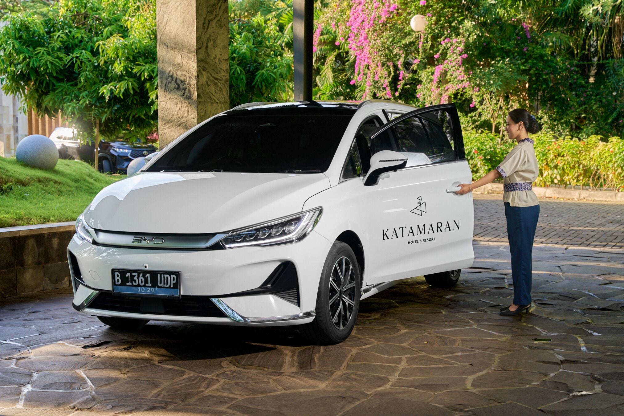 Un SUV blanco con la marca 'KATAMARAN HOTEL & RESORT' estacionado en un área empedrada.