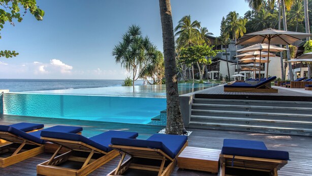 A poolside area with lounge chairs and umbrellas, overlooking a clear blue pool and ocean. - Katamaran Hotel & Resort Lombok (Senggigi)